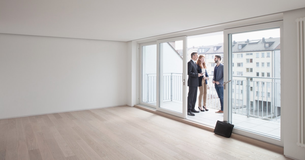 Un agente immobiliare è in piedi con una coppia sul balcone di un appartamento vuoto.