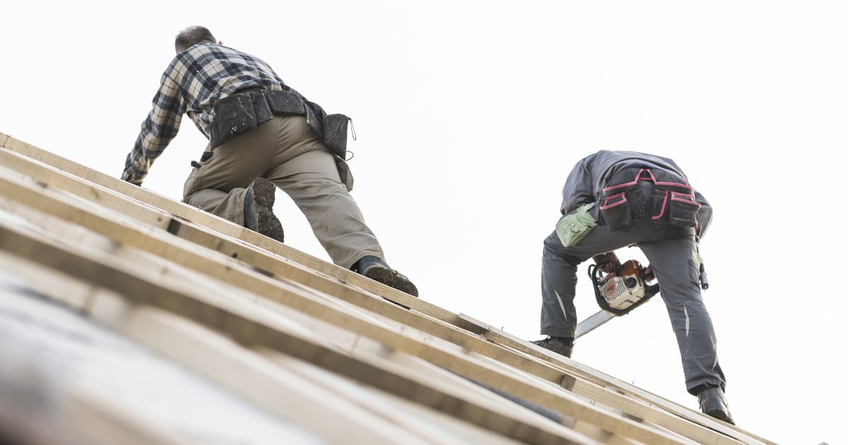 Two construction workers are working on a roof. 