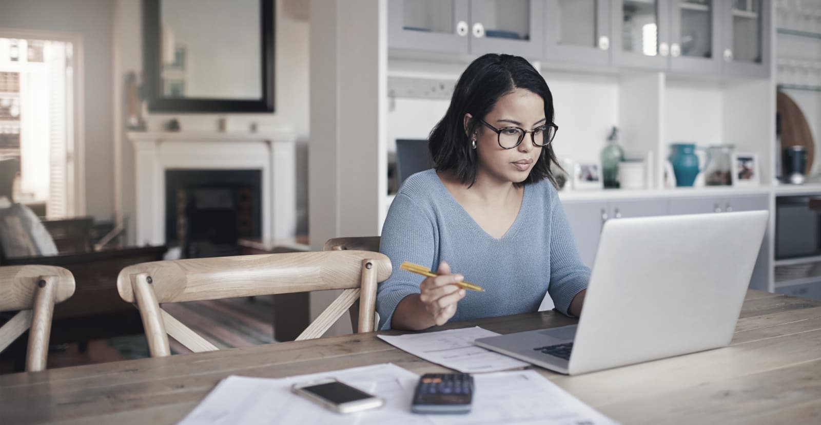 Una donna siede a un tavolo di fronte a un laptop, mentre accanto ha il cellulare, una calcolatrice e dei documenti