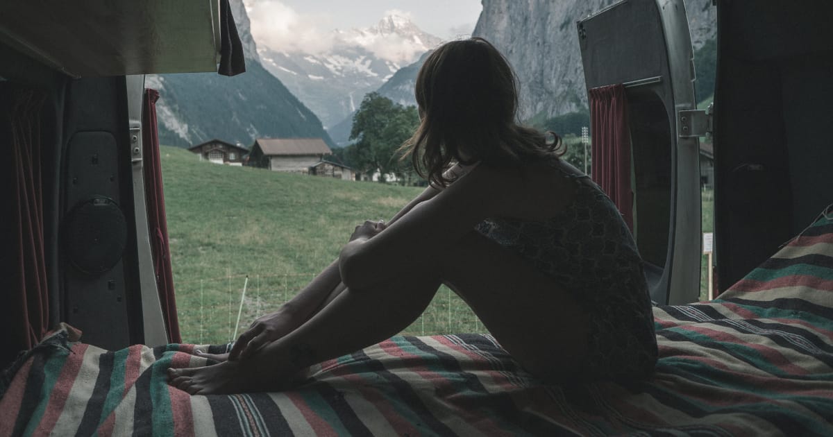 Una giovane donna seduta nel  bagagliaio di un veicolo guarda un paesaggio idilliaco tra le montagne