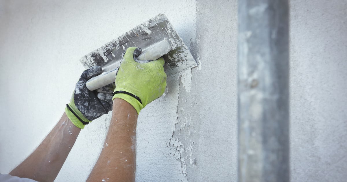 Close-up: Mani con indosso dei guanti applicano dello stucco bianco a una parete.