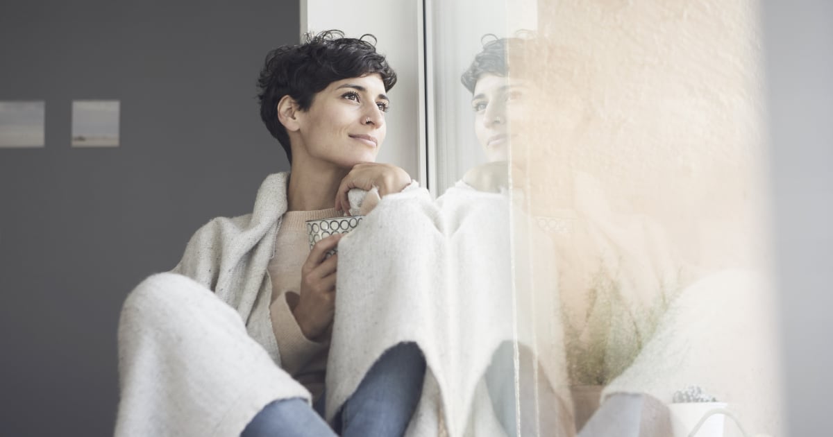 A woman looks pensively out of a window.