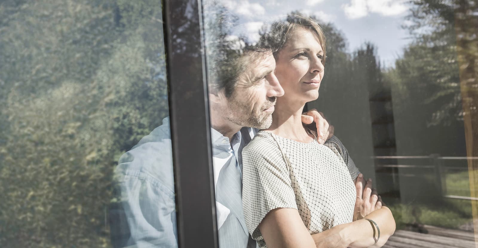 Una coppia si trova all'interno di un edificio con una facciata di vetro e guarda fuori nella natura.