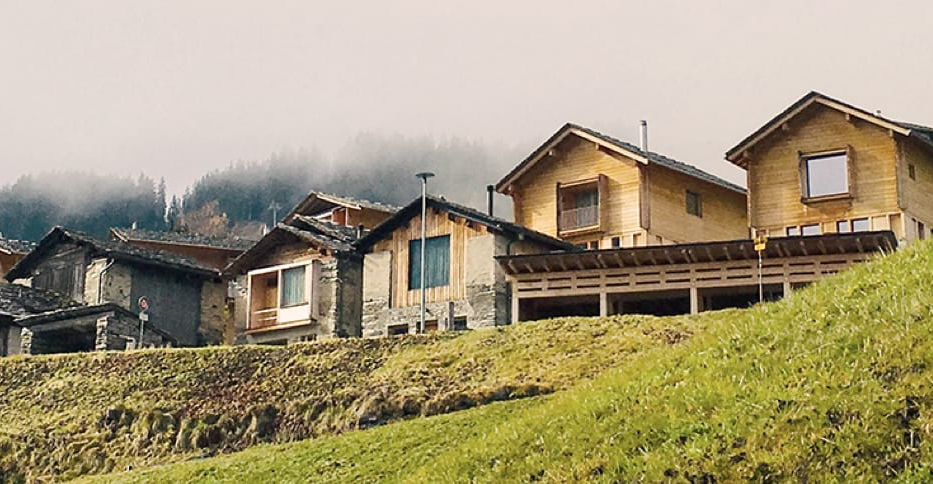 Wooden houses on a slope in front of an alpine mountain landscape