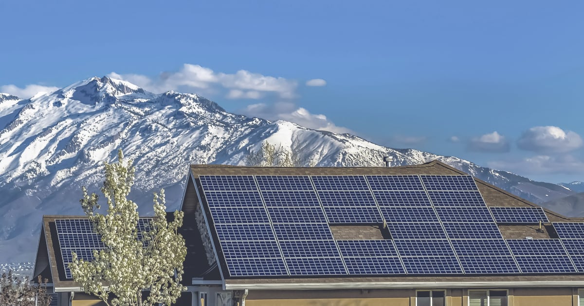 Une maison avec des panneaux solaires se trouve en face d’une montagne. 