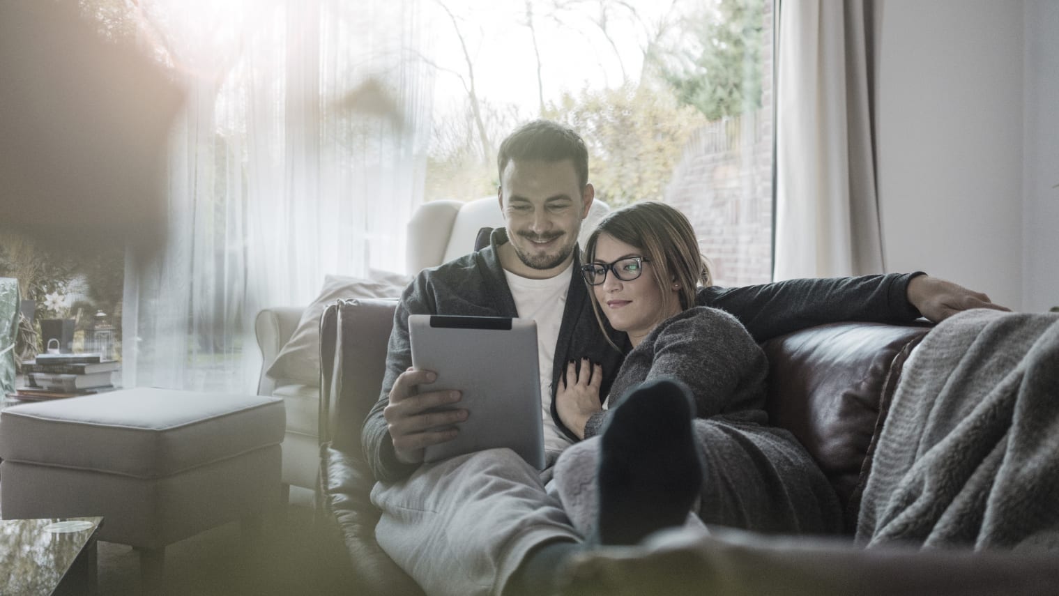 A couple is sitting on a sofa looking at a tablet.