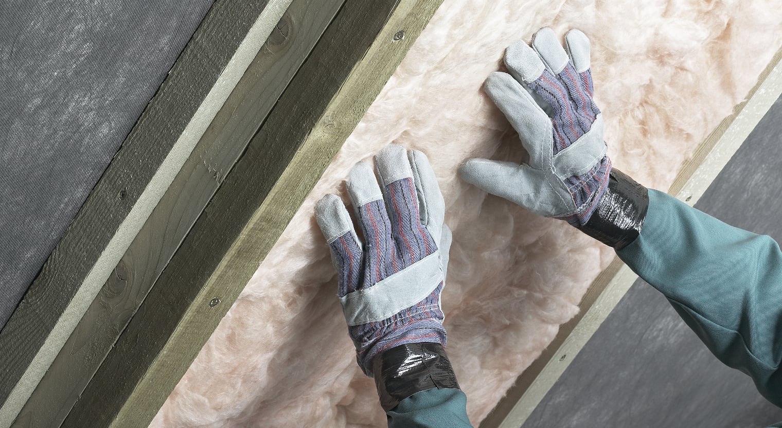 Ein Bauarbeiter setzt Isolationsmaterial ein und trägt dabei Handschuhe.