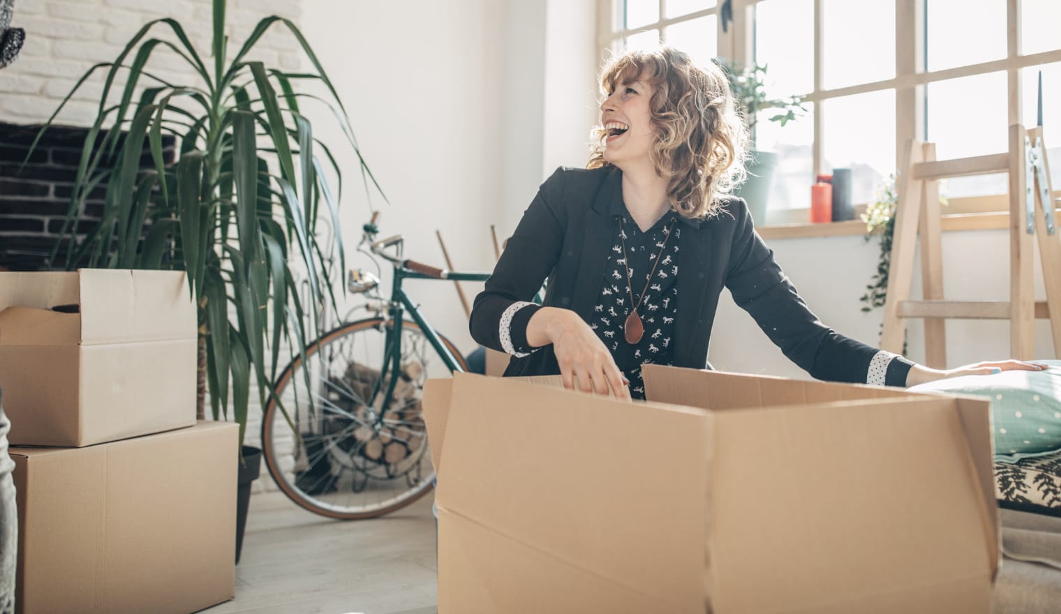 A woman in an apartment laughs as she unpacks a moving box.